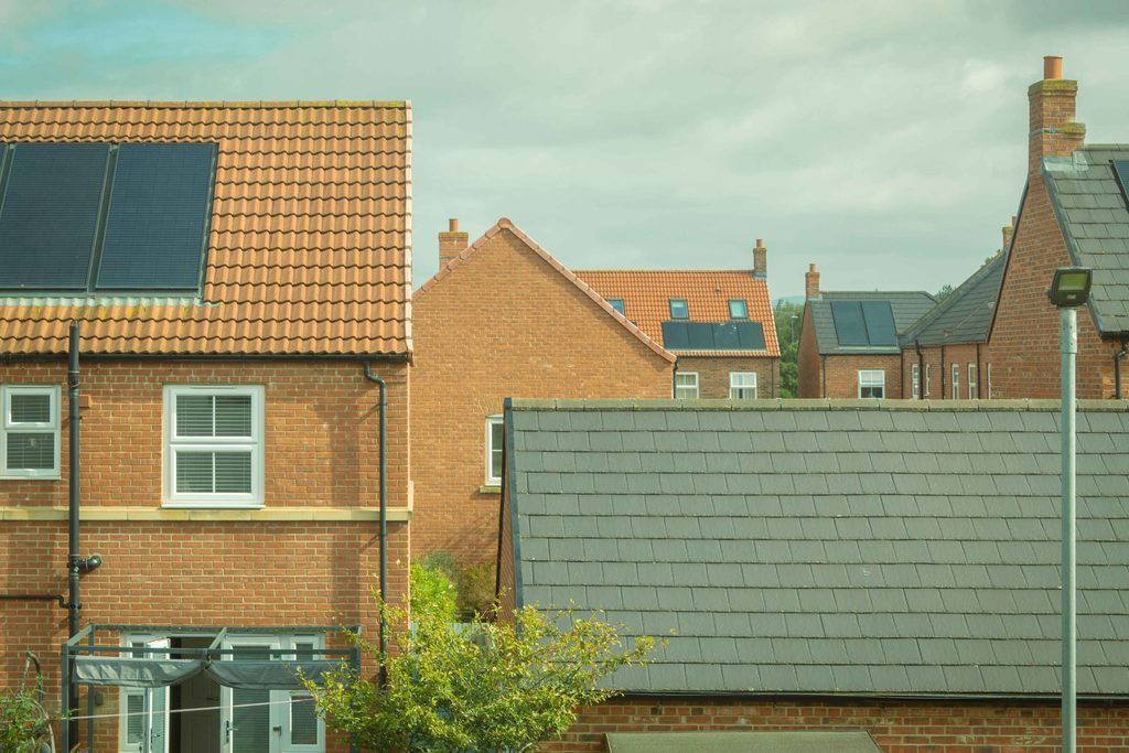 new windows and energy bills | Black Country Glazing Row of red brick houses with tiled roofs and solar panels on several rooftops under a cloudy sky, a streetlamp in the foreground.