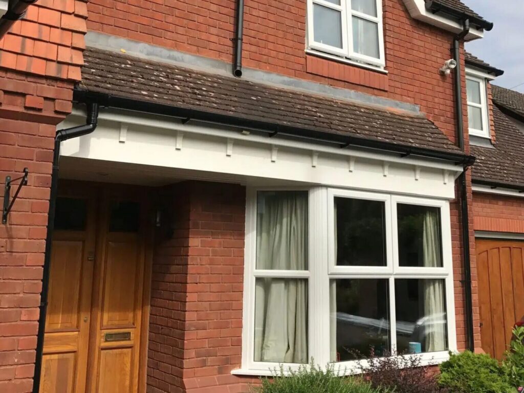 replacement windows from black country | Black Country Glazing Red brick house facade featuring a white-framed bay window, a wooden front door, and landscaped shrubs; sloped tiled roof with dormer windows.